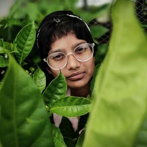 Close-up portrait of a woman partially hidden by lush green leaves outdoors.